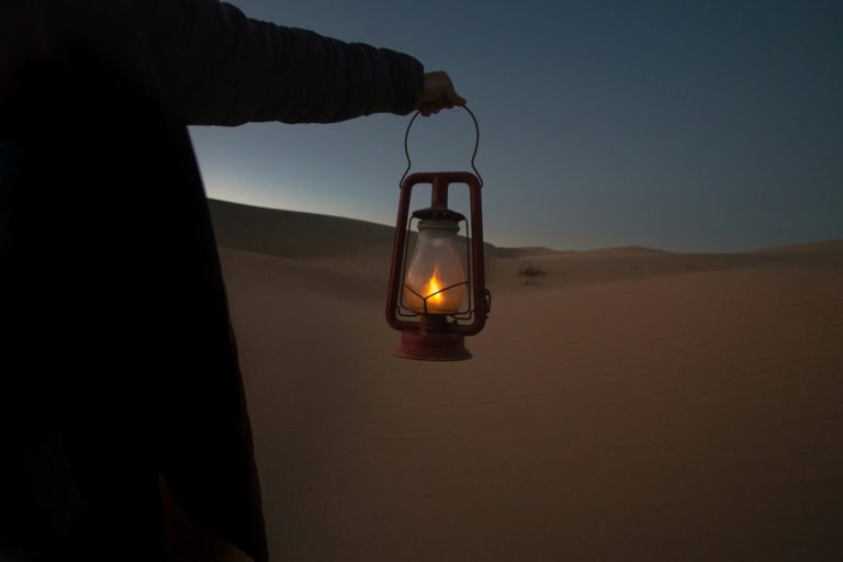 A person holding a lit lantern on a dark hillside shows the importance of discerning truth in a world of misinformation.